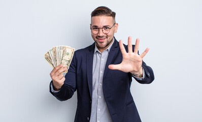 young handsome man smiling and looking friendly, showing number five. dollar banknotes concept