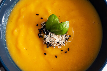 Texture of pumpkin cream soup garnished with sesame seeds and green basil