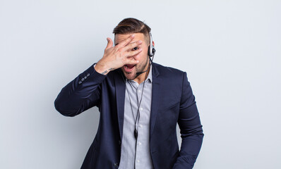 young handsome man looking shocked, scared or terrified, covering face with hand. telearketer...