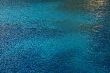 Türkisblaues Meer mit helleren und dunkleren Bereichen und leichter goldener Reflexion Querformat