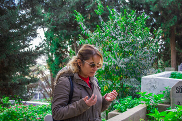 Blonde haired woman with glasses prays at the cemetery