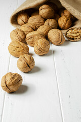 Lots of walnuts in a burlap bag. Wooden white background. Copy space