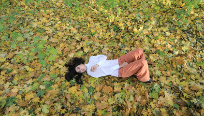 autumn portrait of a beautiful brunette lying on the grass with leaves