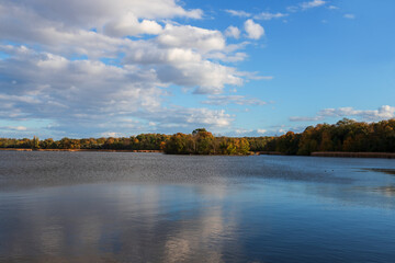 A large pond in which the sky is reflected. There are colorful trees around the pond.