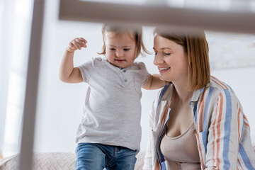 Smiling mom near daughter with down syndrome at home.