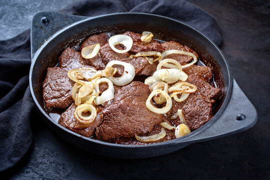 Traditional Filipino dry aged angus bistek tagalog steak with onion rings in soy sauce served as close-up in a cast-iron casserole