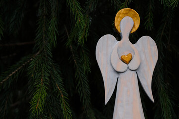 Golden heart in angel hands. Light angel on a dark background. Wooden figurine. Spruce background....