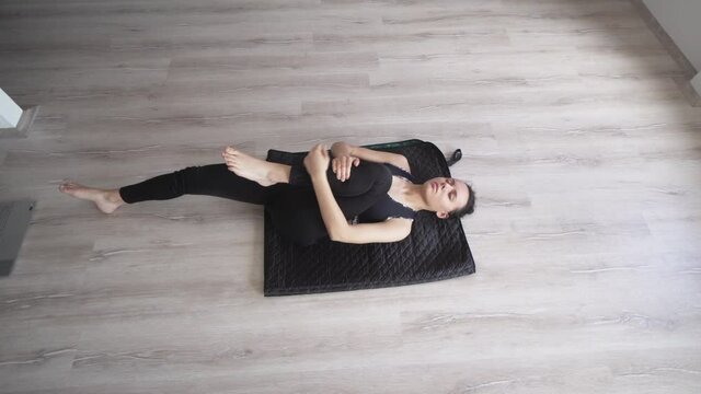 Young happy woman wearing  sportswear lying on floor practising half knees to chest pose. Meditating yoga concept