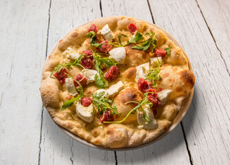 Pizza with mozzarella cheese, raw sausage and rocket in plate on white wooden board table