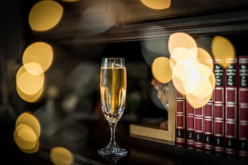 Fototapeta na wymiar Side view of full champagne glass in front of classy bookshelf with row of books titled 