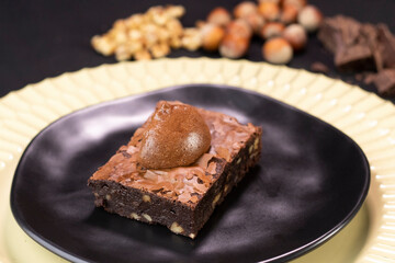 Chocolate Brownie with nuts and chocolate cream on black plate