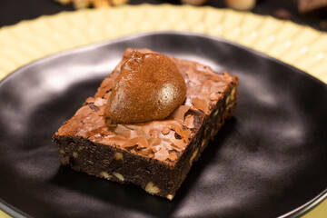 Chocolate Brownie with nuts and chocolate cream on black plate