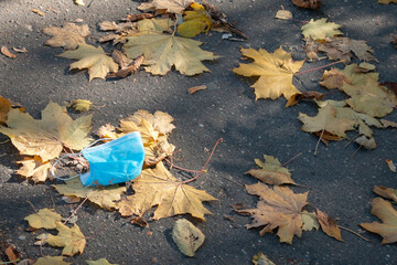 A disposable used blue medical mask is thrown to the ground. Concept of modern version of...