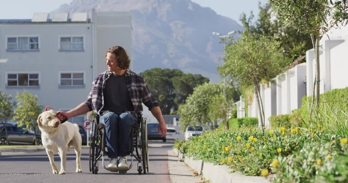 Smiling caucasian disabled man in wheelchair taking his pet dog for a walk in street