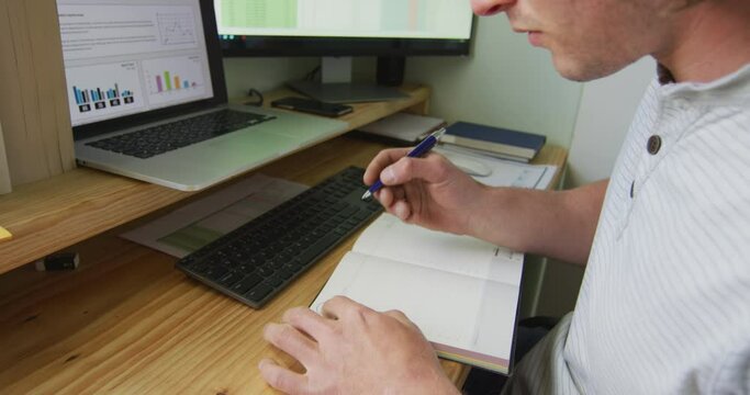 Focused caucasian man working remotely using computer, taking notes