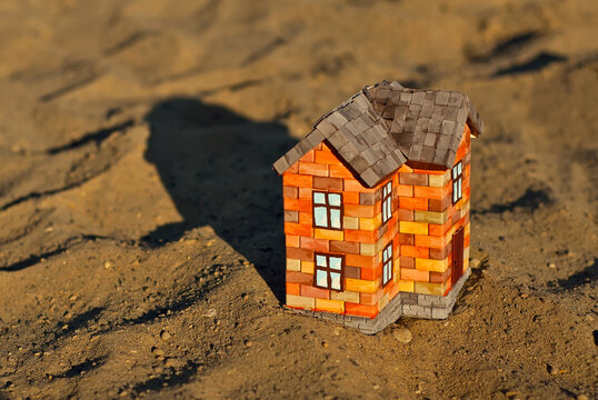 Іграшковий будиночок з цегли на піску. Помаранчевий будинок на коричневій землі. Концепт власного житла та будівництва.