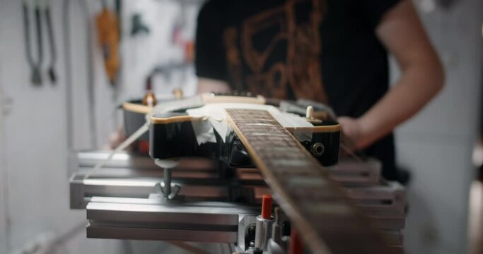Luthier mounts electric guitar on the jig at the musical instruments repair shop, 4k 60p 10 bit