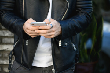 Cropped view of fashionable man in leather jacket using cellphone outdoors 
