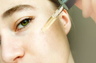 Close-up portrait of woman applying glass peep liquid, skin texture. Apply a tea tree moisturizing...
