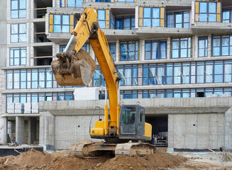 Photo of an excavator at the construction site of multi-storey buildings in the city