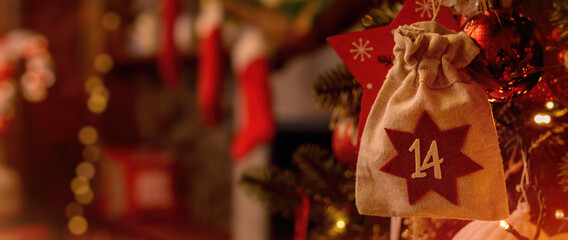 Fototapeta na wymiar Christmas background. Advent calendar. Advent calendar in the form of an eco bag hangs on the Christmas tree against the background of the Christmas room with a fireplace and Santa's boots.. Banner