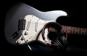 Silver electric guitar with headphones isolated on black background - obrazy, fototapety, plakaty