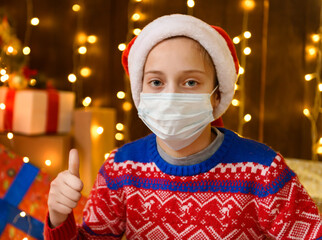 Child girl as Santa helper posing in new year decoration. Wearing a protective face mask against...