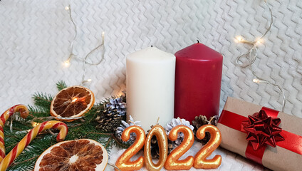 white and red candles, dried orange slices, golden fir cones, a Christmas caramel stick and a gift box made of eco-paper decorated with a red ribbon. the inscription 2022 in the foreground
