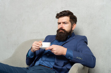 Bearded man relax drinking tea or coffee in rest armchair during work break, relaxing