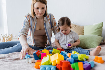 Parent and child with down syndrome playing colorful building blocks on bed at home.