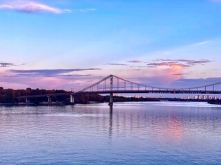 Bay bridge at night over the river. Pedestrian crossing bridge across Dnieper river against the background of evening sunset. Beautiful views of Kiev city at night.