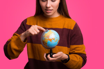 Wonderful young girl is pointing on the Earth globe she is holding.