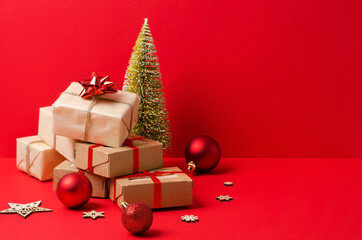 A stack of gifts in kraft paper and kraft boxes on a red background with wooden eco decorations for the Christmas tree. Christmas background, boxing day, Christmas gifts