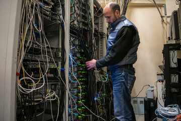 Maintenance of network Internet equipment in the data center rack. A technician is laying wires in a server room rack.