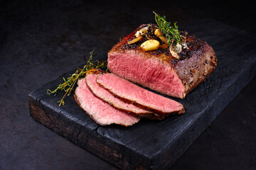 Traditional Commonwealth Sunday roast with sliced cold cuts roast beef with garlic and salt as close-up on a rustic charred wooden board - obrazy, fototapety, plakaty