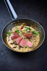 Traditional barbecue dry aged angus roast beef steak natural with mushrooms and onions in cream sauce served as close-up in a classic skillet