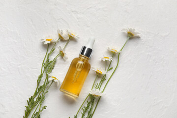 Bottle of essential oil and chamomile flowers on light background