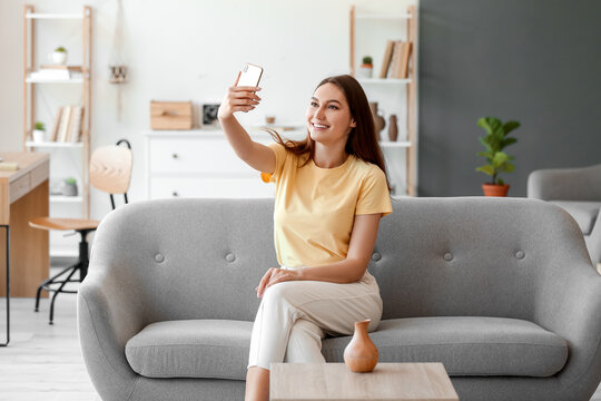Young smiling woman sitting on sofa and taking selfie