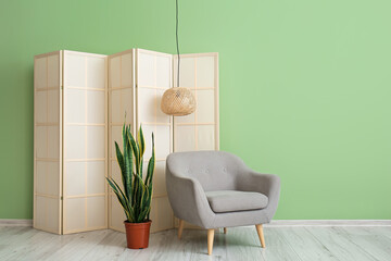 Grey armchair with houseplant and folding screen near green wall