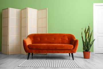 Red sofa, houseplant and folding screen near green wall