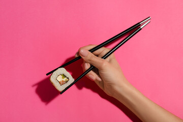 Woman holding chopsticks with tasty maki roll on color background © Pixel-Shot