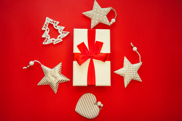 White Christmas gift box with red ribbon and Christmas decorations on a red background.