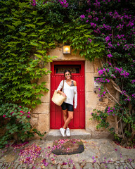 Beauty model 80s fashion girl with green sunglasses posing at a classic red door with many flowers in an old house town in costa brava