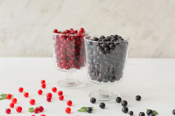 Bowls with tasty red and black currants on light background