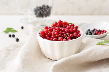 Bowl with tasty red currants on light background