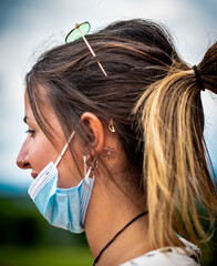 side profile photo from a girl with blue mask and sunglasses and a sunny tatto behind the ear