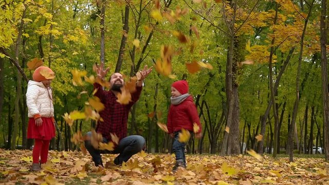 Two happy funny family daddy children kids have fun in park with dad father enjoying autumn fall nature weather. Kid Collect throw up leaves in baskets spend time together playing on forest landscape