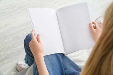 Woman reading blank magazine on light background
