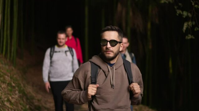 Group of adult male tourists or travelers walking through highland forest. Crowd of hiking guys in autumn woods among trees. Young Caucasian men on camping tourism trip. Recreation activity in nature.