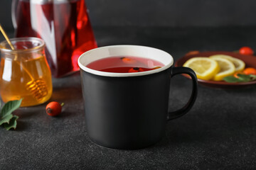 Cup of tasty rose hip tea and berries on black background